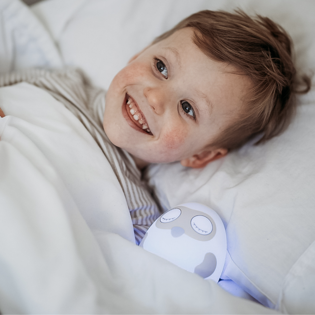 Ooly sleep training clock with blue glow in bed with boy