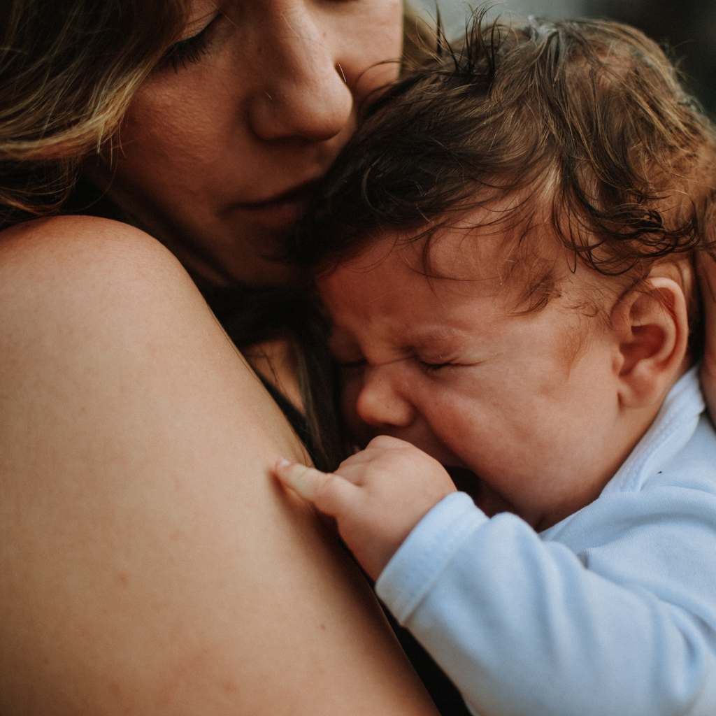 Crying baby cuddling with mum