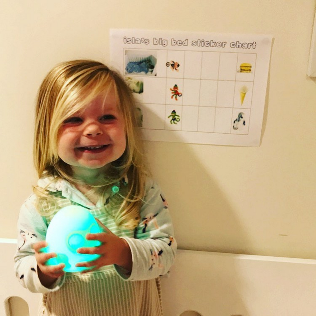 Girl holding Ooly sleep training clock with a green glow 