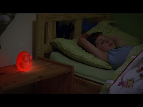 Girl lying in bed with red glow Ooly sleep clock next to her